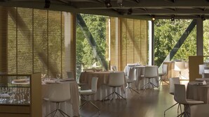 Un comedor con mesas dispuestas para comidas, ventanas amplias con persianas y vistas a zonas verdes.