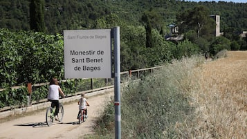 Un panneau indiquant « Sant Fructiu de Bages » et « Monestir de Sant Benet de Bages », le long d’un sentier bordé de verdure, avec une colline en arrière-plan.