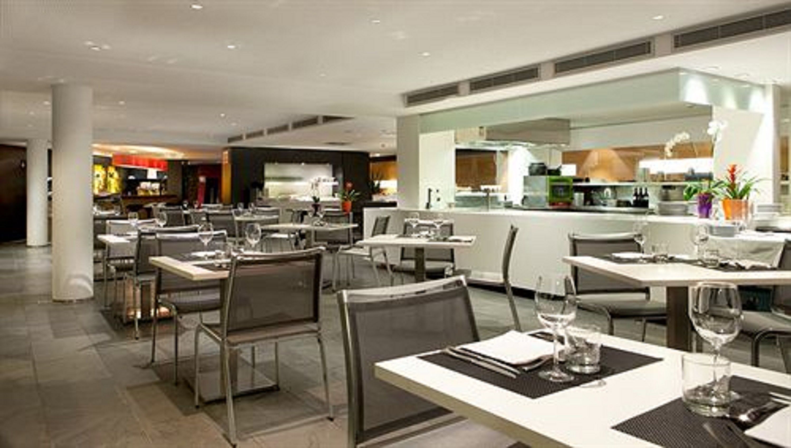 Un restaurante moderno con varias mesas y sillas, una barra central y una cocina visible al fondo.