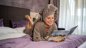 Uma pessoa deitada na cama com um cobertor roxo, lendo um livro.