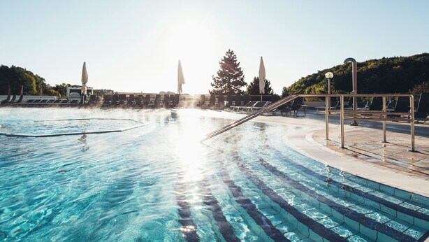 Una piscina con agua cristalina, iluminada por el sol, rodeada de sillas de descanso y sombrillas.