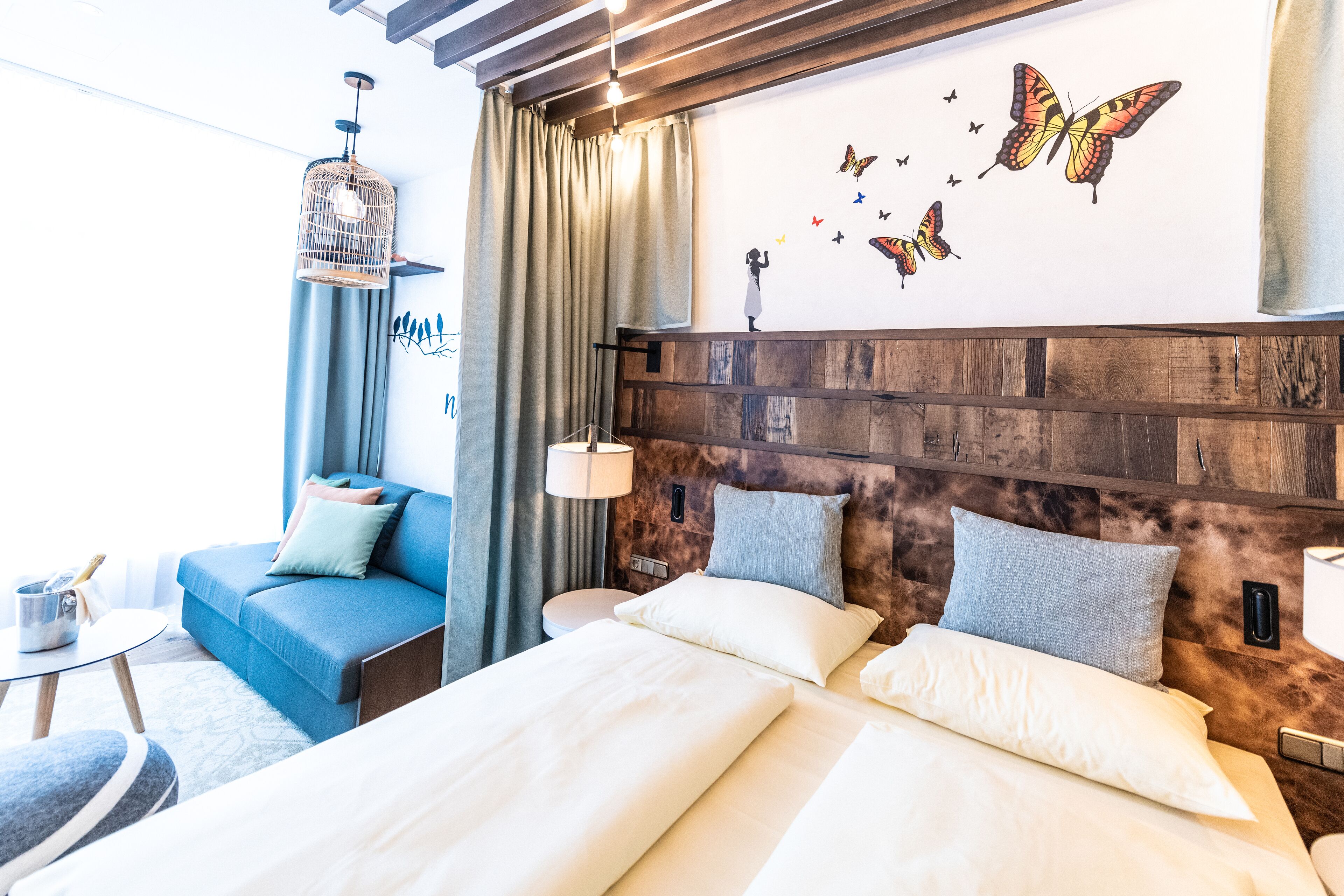 A hotel room with a bed, a blue sofa, a wooden headboard, and a wall with butterfly decals.