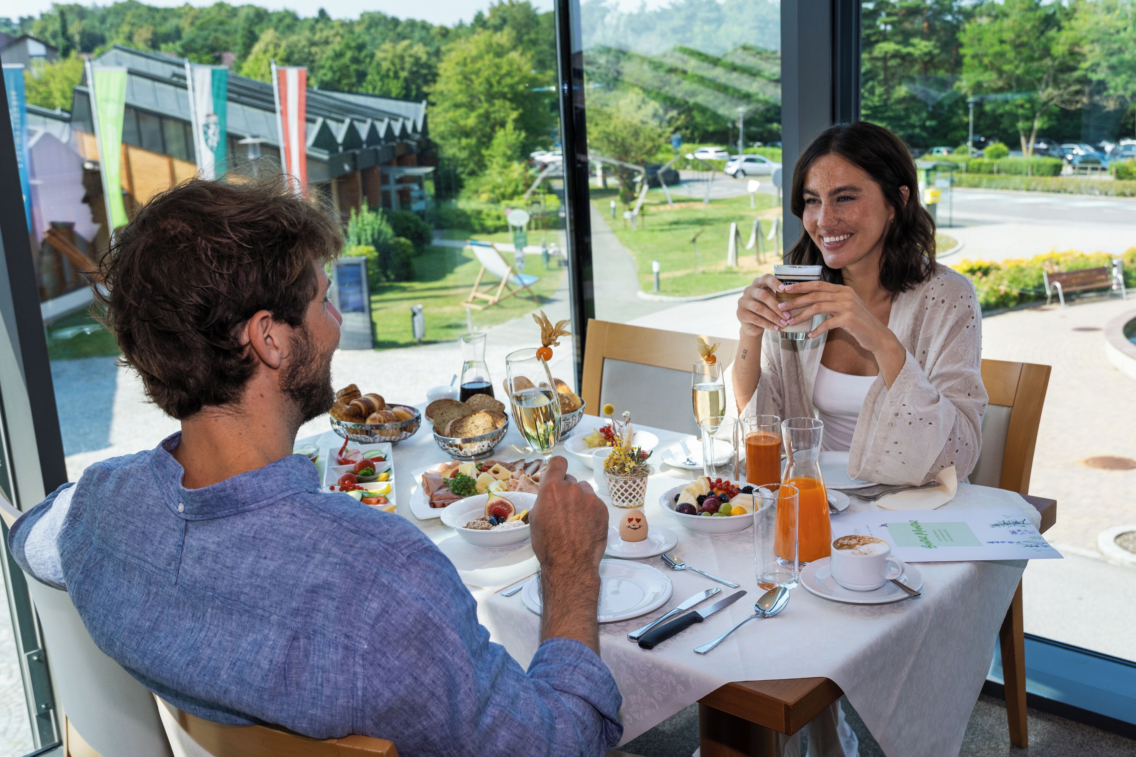 A dining table set with breakfast items, including bread, fruit, and beverages, in a room with a view of a green landscape.