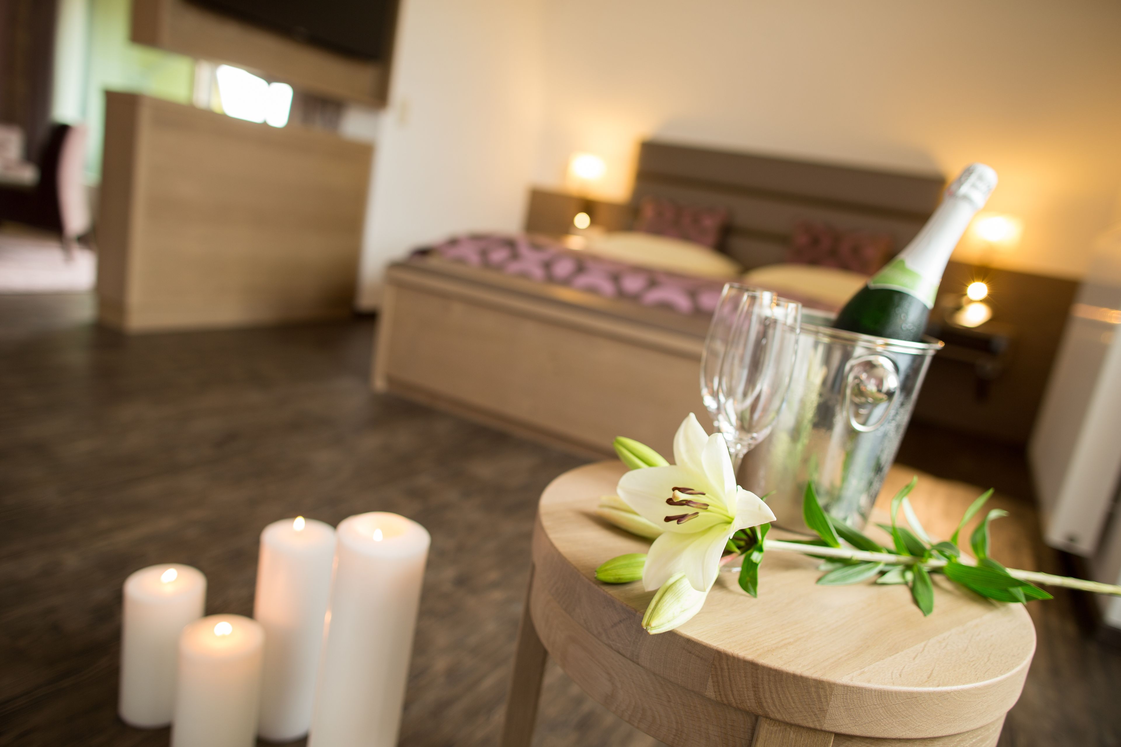 Un taburete de madera con una botella de champán, copas y una flor blanca en una habitación de hotel.