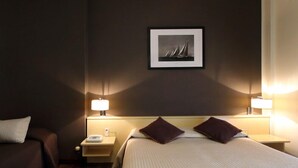 Una habitació d'hotel amb un llit, dues taules de nit, dues làmpades, una petita taula i un quadre al mur.