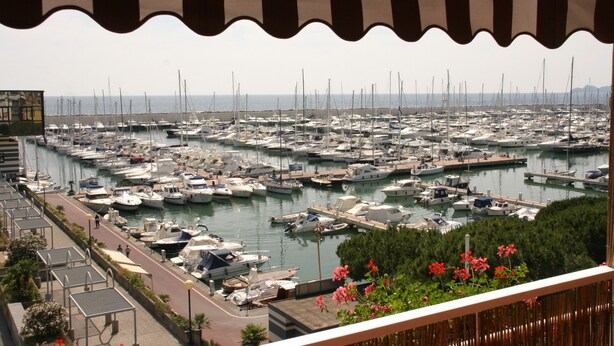 Un port esportiu amb nombroses embarcacions amarrades, un camí al costat de l'aigua i vista al mar.