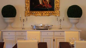 Zona de dinar amb una taula de buffet blanca, dues plantes en testos, un quadre amb marc daurat i un candelabrum.