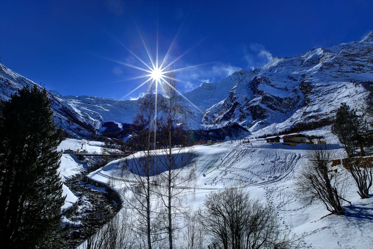 A snow-covered mountain landscape with a clear sky and a bright sun.