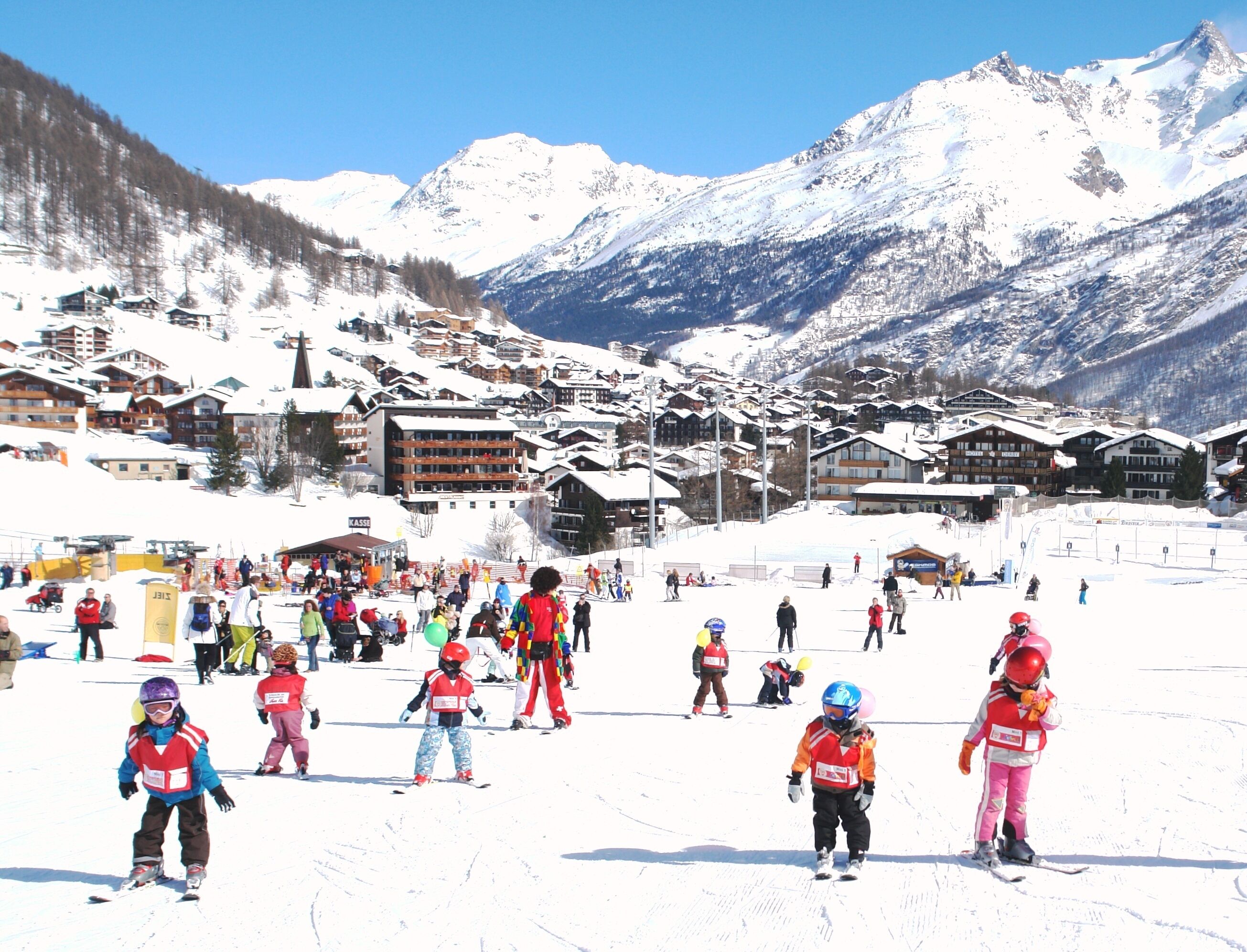 A ski resort with snow-covered slopes, buildings, and mountains in the background.