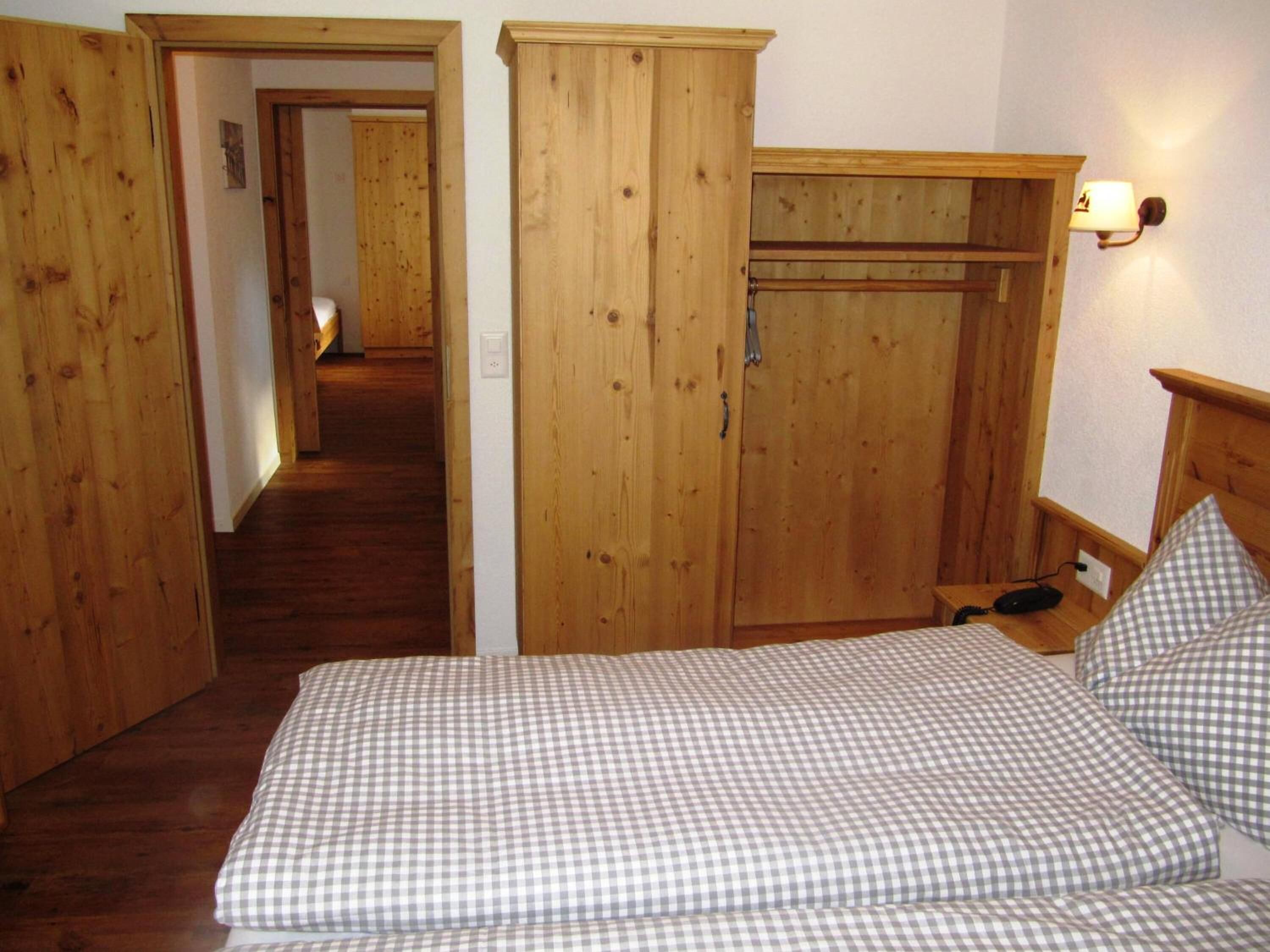 A bedroom with a checkered bedspread, wooden wardrobe, and a nightstand with a lamp.