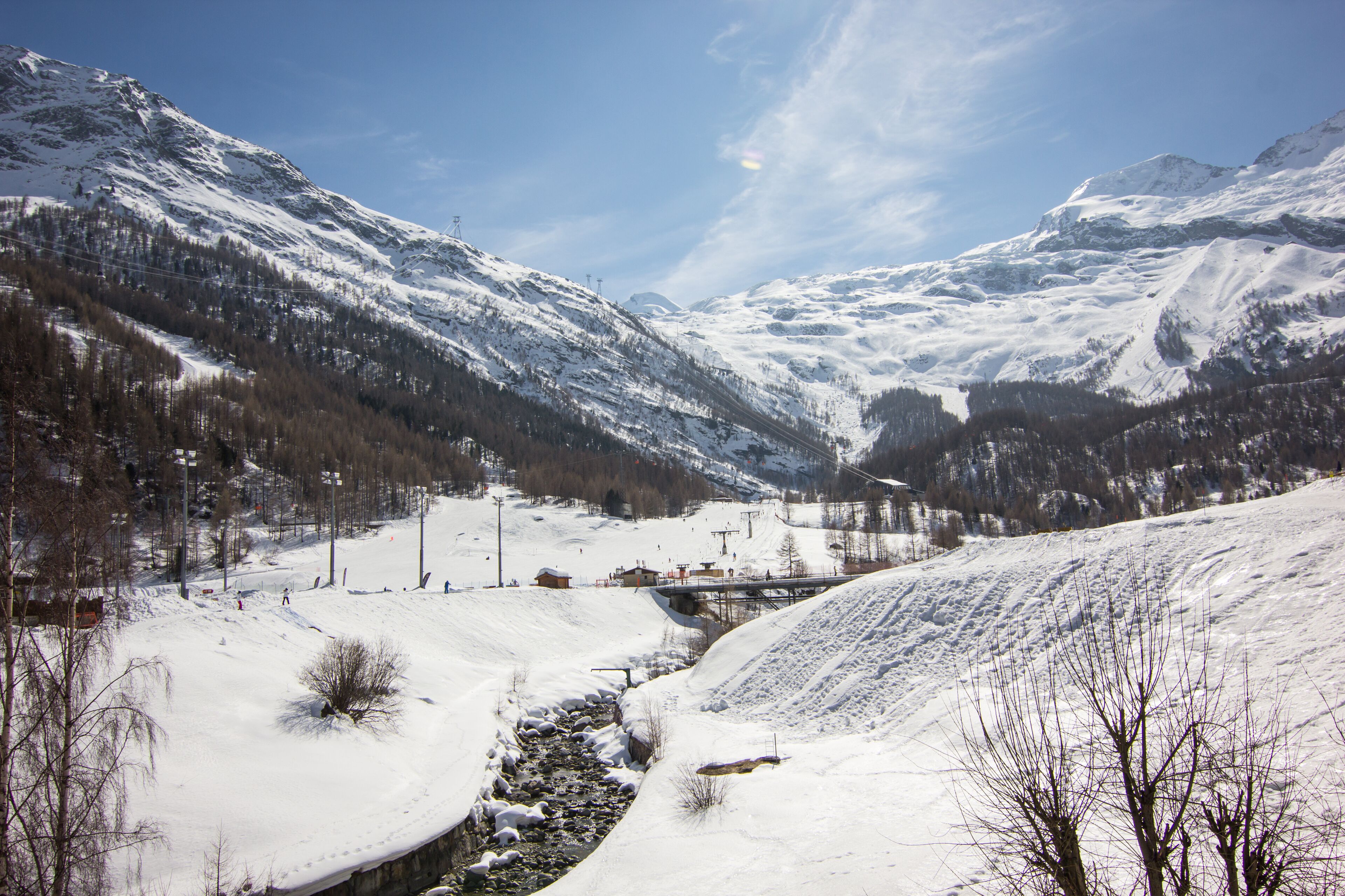Un paisaje montañoso nevado con un río, edificios y un puente.