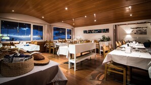A restaurant with wooden ceilings and large windows overlooking a snowy landscape. Tables are set with white tablecloths and various dishes. - Hotel Bristol (Saas-Fee)