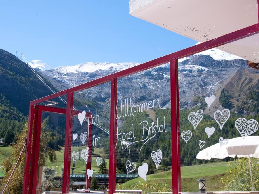 Ein Hotel Eingang mit Bergpanorama, mit rotem Rahmen und herzförmigen Dekorationen an den Scheiben.