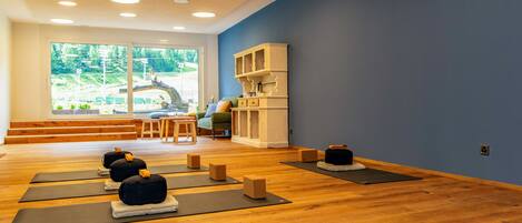 Estudio de yoga con pisos de madera, tapetes de yoga, bloques y vistas a la montaña a través de amplias ventanas.
