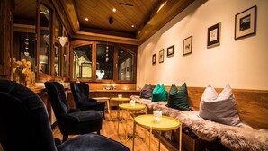A cozy lounge area with plush seating, wooden accents, and framed pictures on the wall. - Hotel Bristol (Saas-Fee)