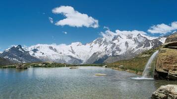 Un lago de montaña con aguas cristalinas, una cascada y picos nevados bajo un cielo azul.