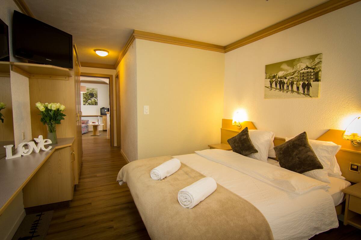 A hotel room with a bed, bedside lamps, a TV, a painting, and a 'Love' sign on the wall.