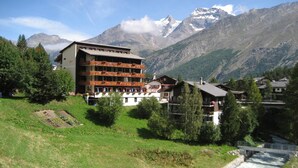 A hotel with multiple balconies, a river, and mountains in the background. - Hotel Bristol (Saas-Fee)