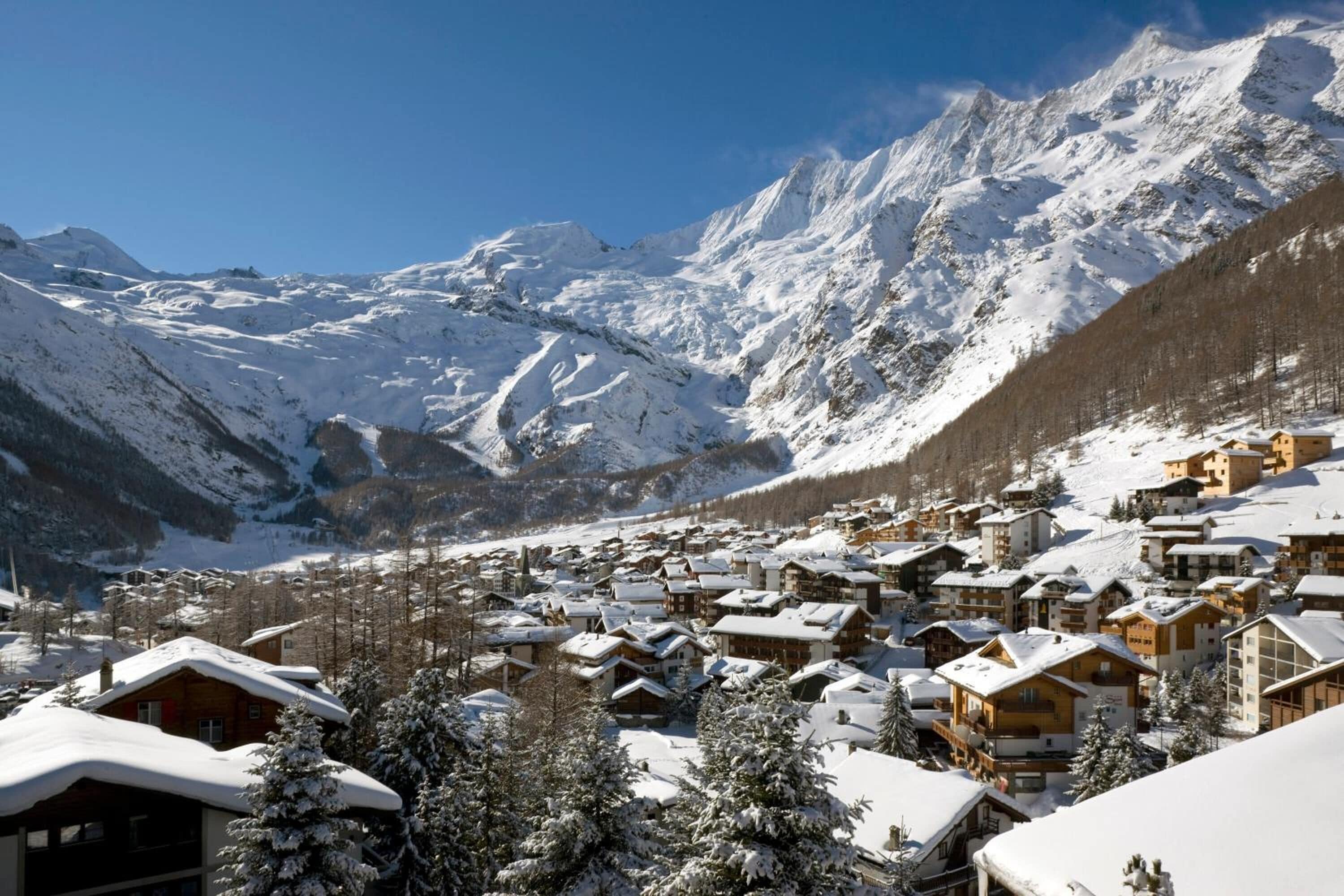 Ein verschneites Bergdorf mit Holzhäusern und freiem Blick auf die Berge.