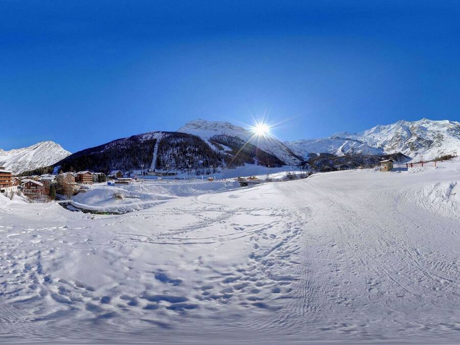 Pista de esquí nevada con edificios y una montaña al fondo.