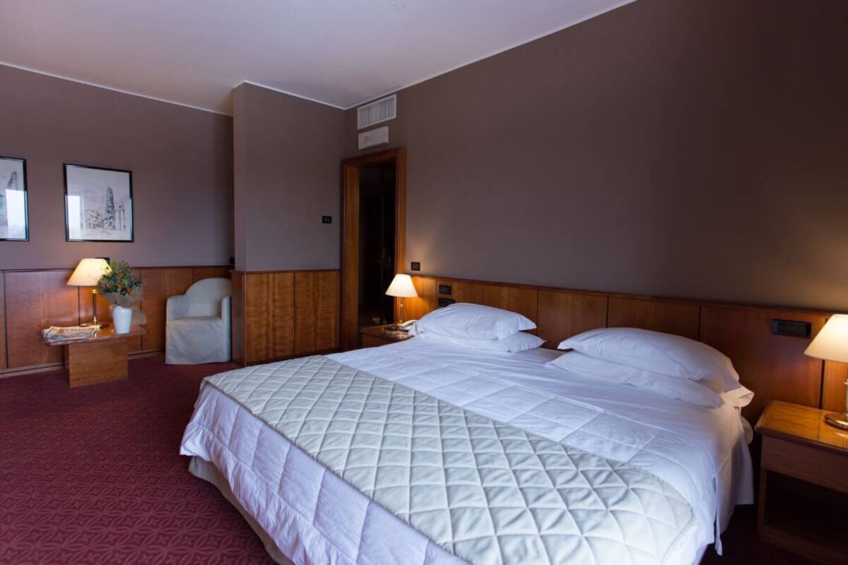 A hotel room with a large bed, two bedside tables with lamps, a chair, and framed pictures on the wall.