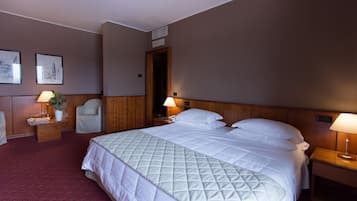 Ein Hotelzimmer mit einem großen Bett, zwei Nachttischen inklusive Lampen, einem Sessel und gerahmten Bildern an der Wand.