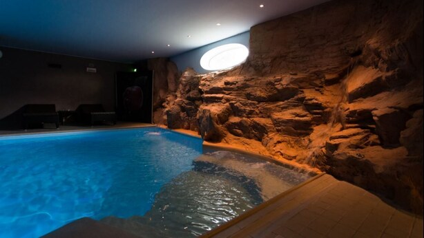 Una piscina interior con pared rocosa y tragaluz circular.