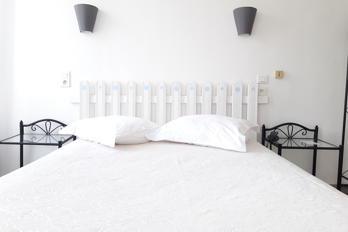 Een bed met witte beddengoed, een wit hoofdeinde, twee nachtkastjes en twee wandlampen.