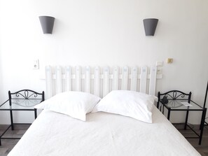 A bed with white bedding, a white radiator, two black metal nightstands, and two wall-mounted lamps.