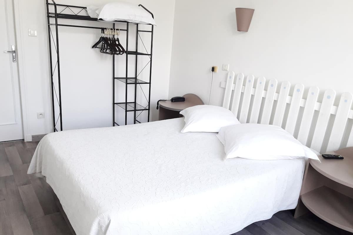 Un dormitorio ordenado con cama, mesita de noche, silla, armario y radiador.