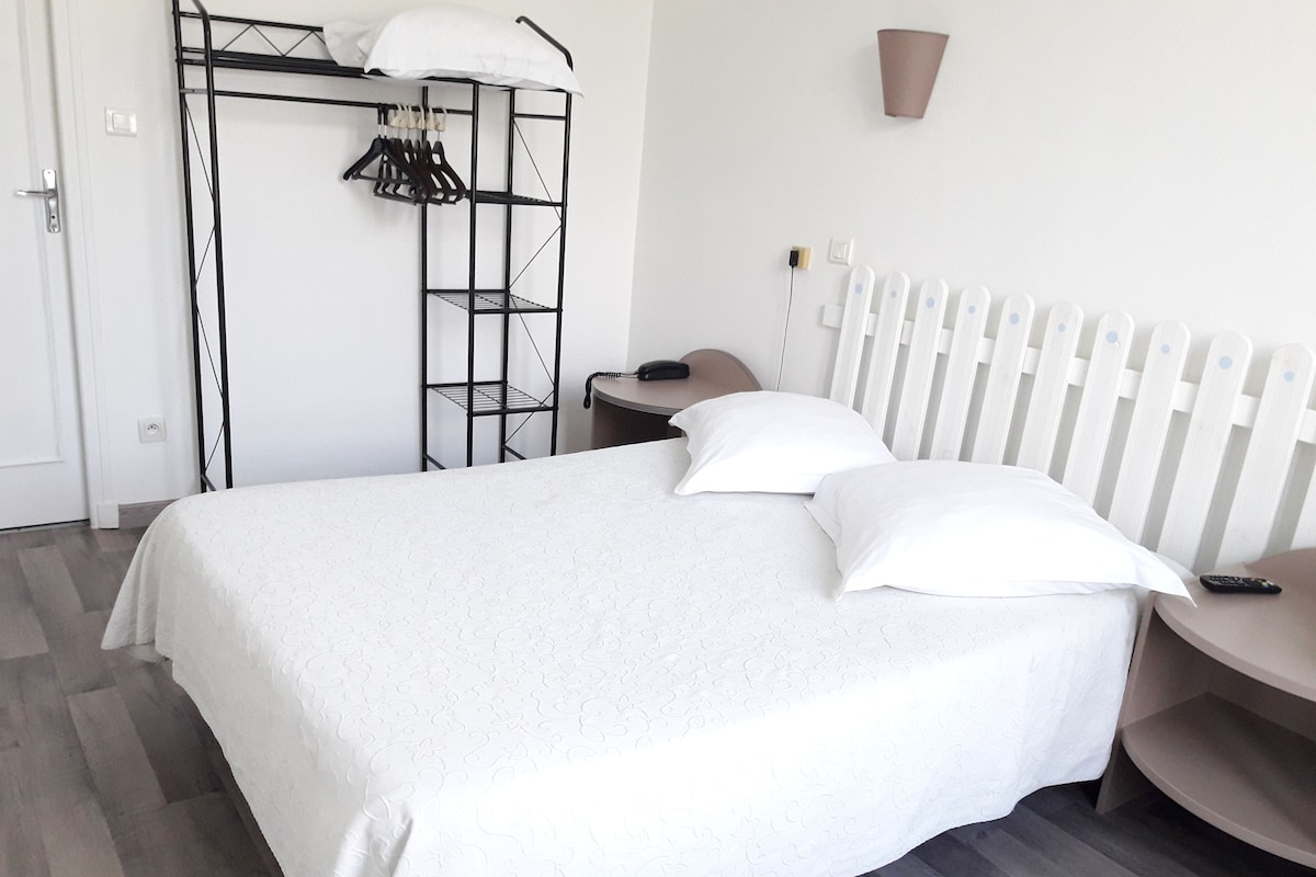 Een netjes ingerichte slaapkamer met een bed, nachtkastje, stoel, kast en radiator.