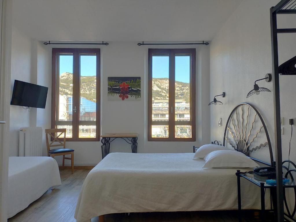 A bedroom with a bed, a chair, a desk, and a TV. There are two windows with a view of the outside.