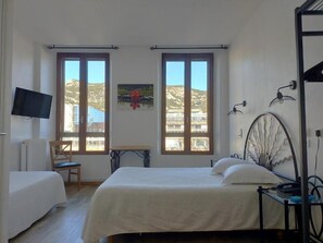 Een slaapkamer met een bed, een stoel, een bureau en een televisie. Er zijn twee ramen met uitzicht op het omliggende landschap.