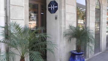 A hotel entrance with a sign indicating it is a hotel. There are two large blue planters with palm trees in front.