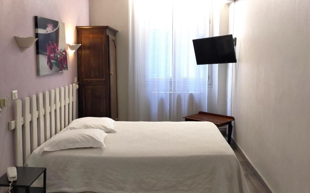 A bedroom with a bed, a bedside table, a nightstand, a wall-mounted TV, and a window with curtains.