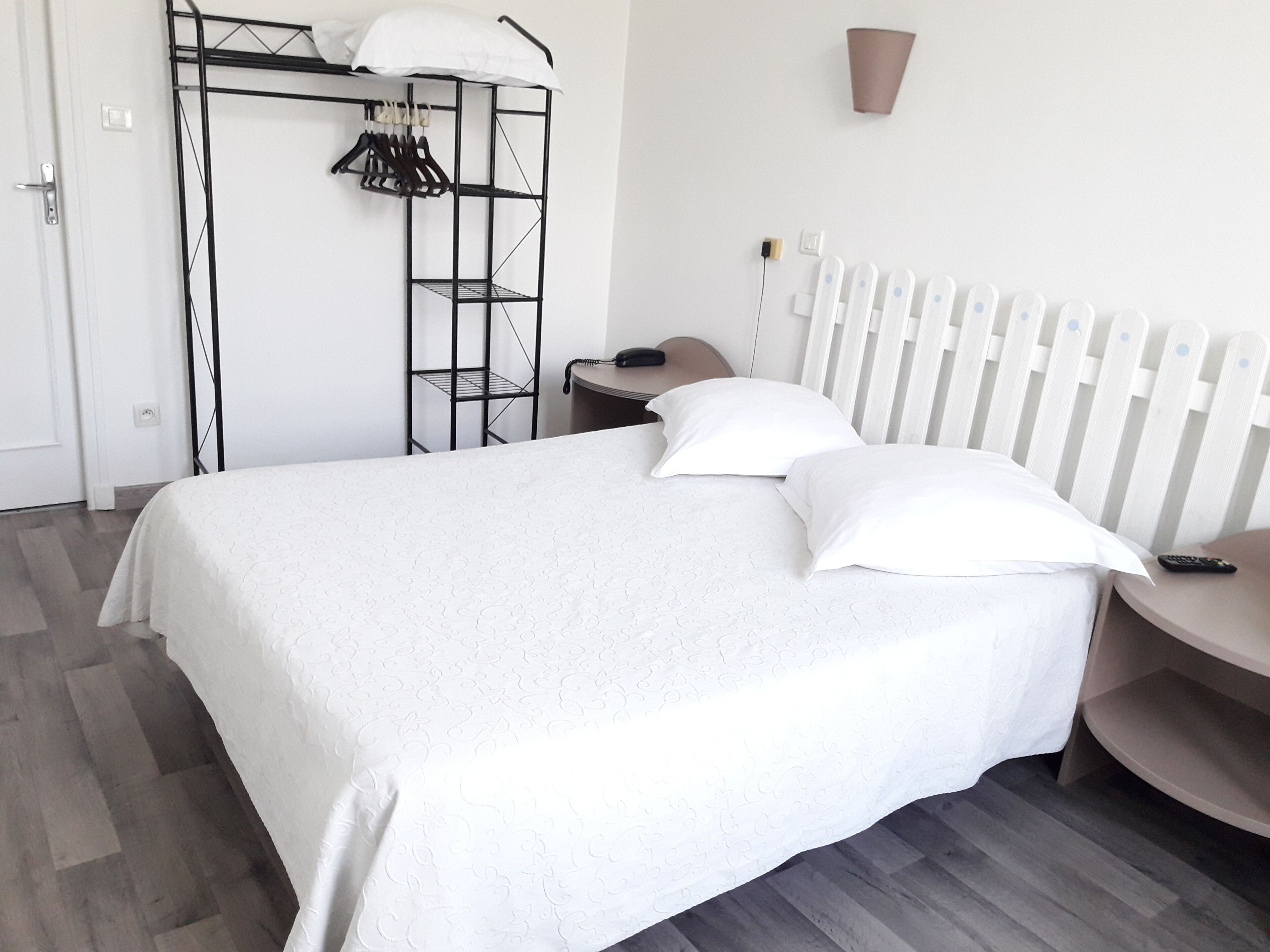 Un dormitorio ordenado con cama, mesita de noche, silla, armario y radiador.