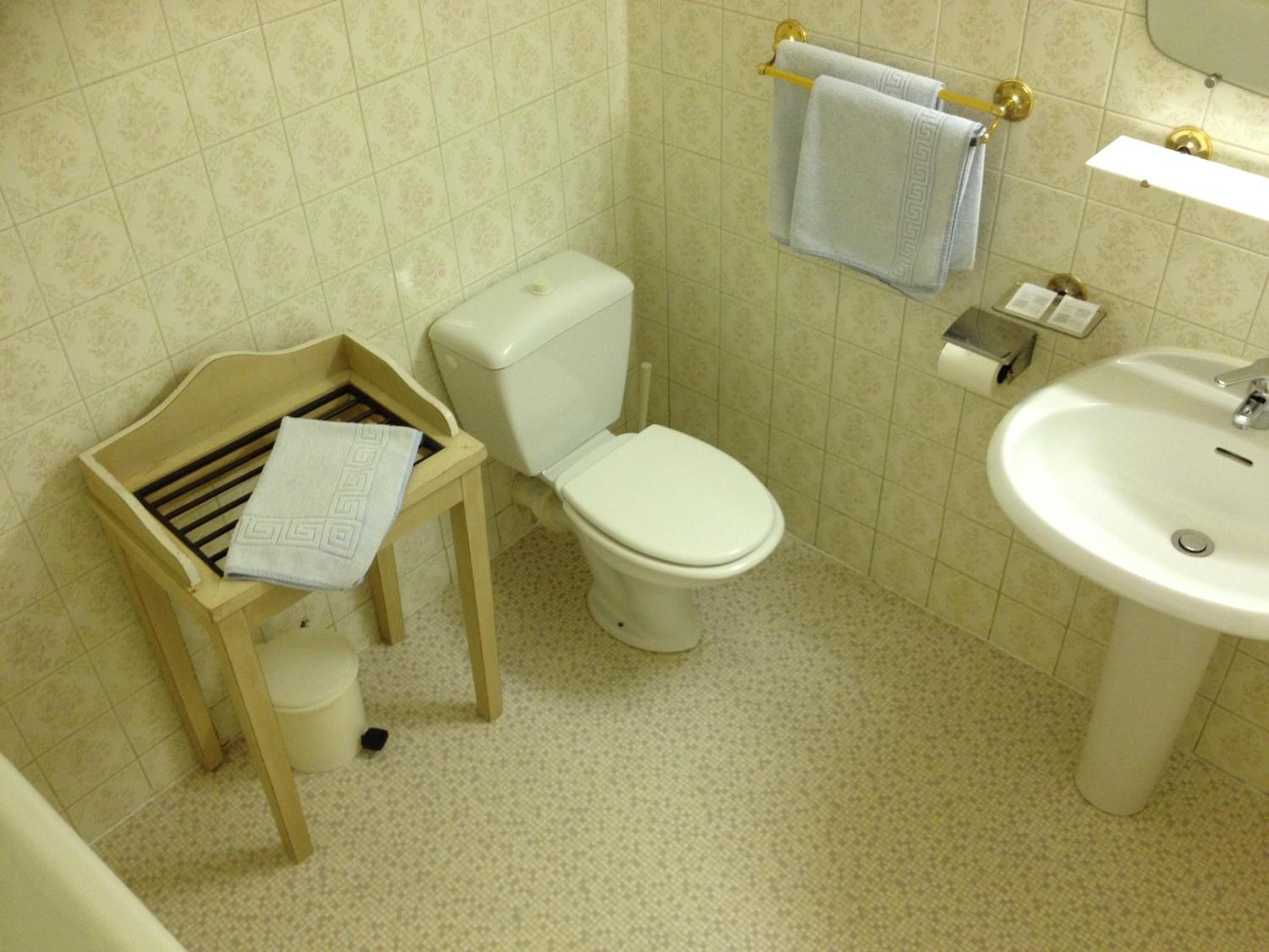 A bathroom with a toilet, a sink, and a wooden bench with a towel.