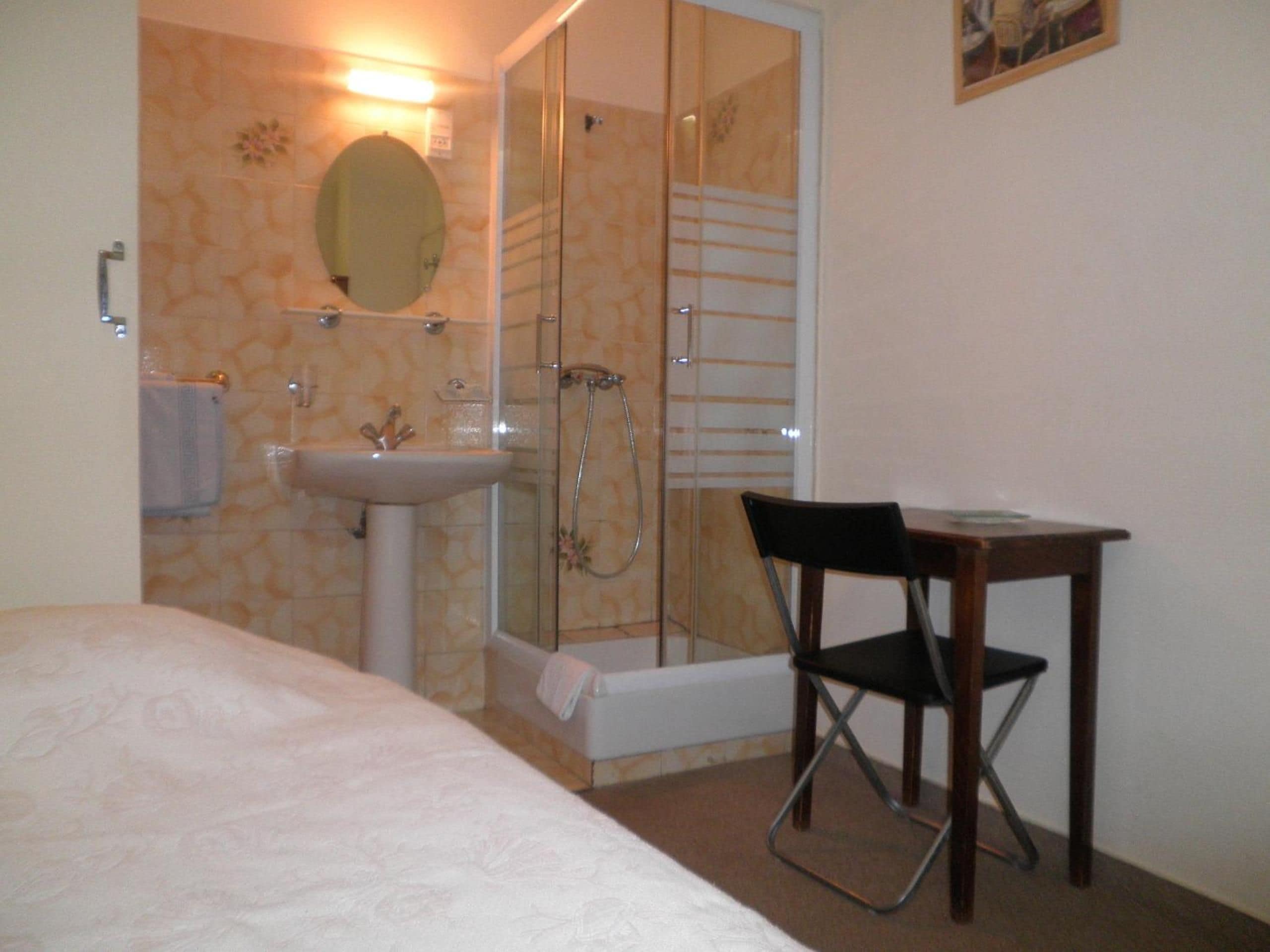 A hotel bathroom with a shower, sink, and a small table with a chair.