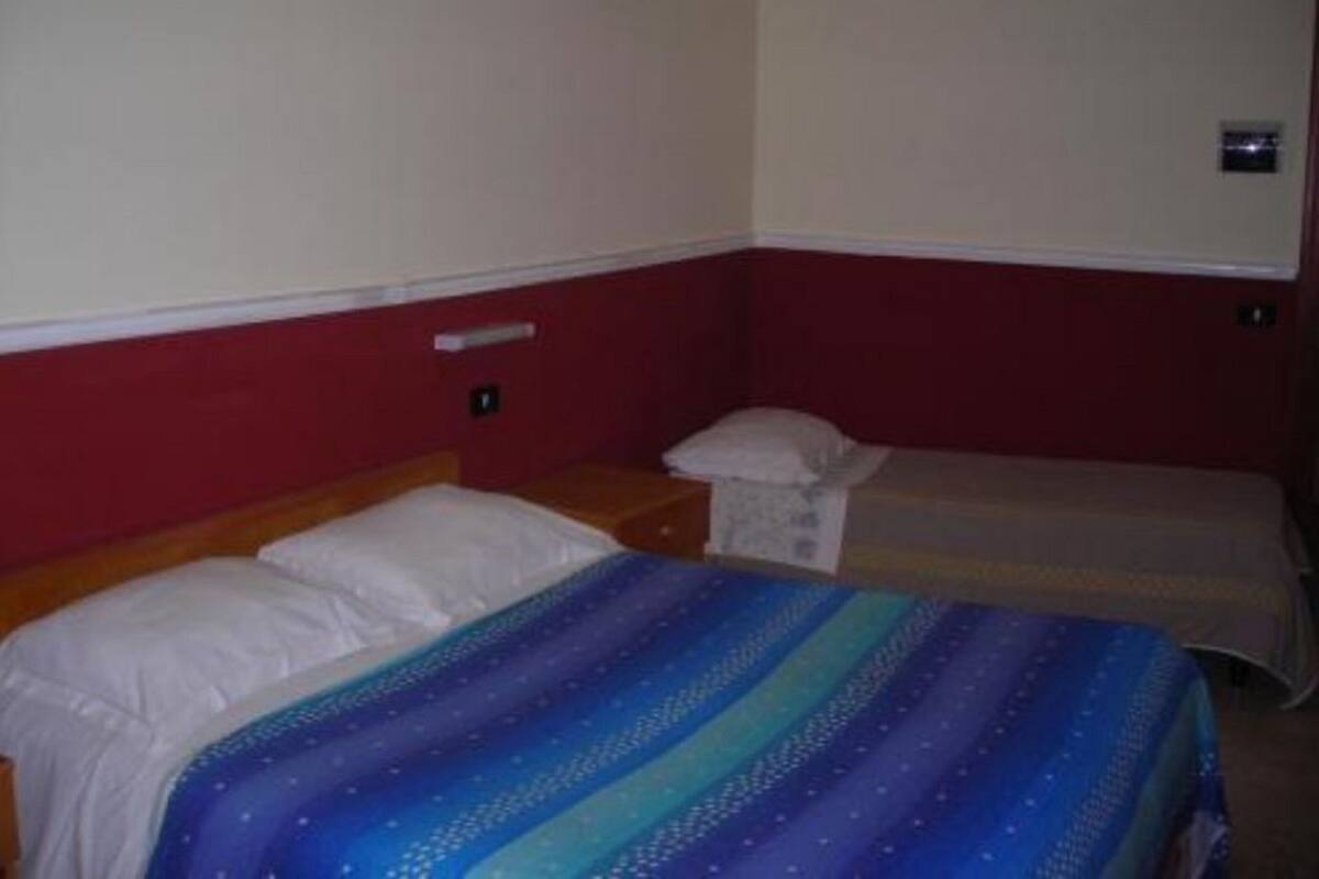 Une chambre avec un lit simple, une tête de lit en bois, une table de chevet et une petite lampe de chevet.