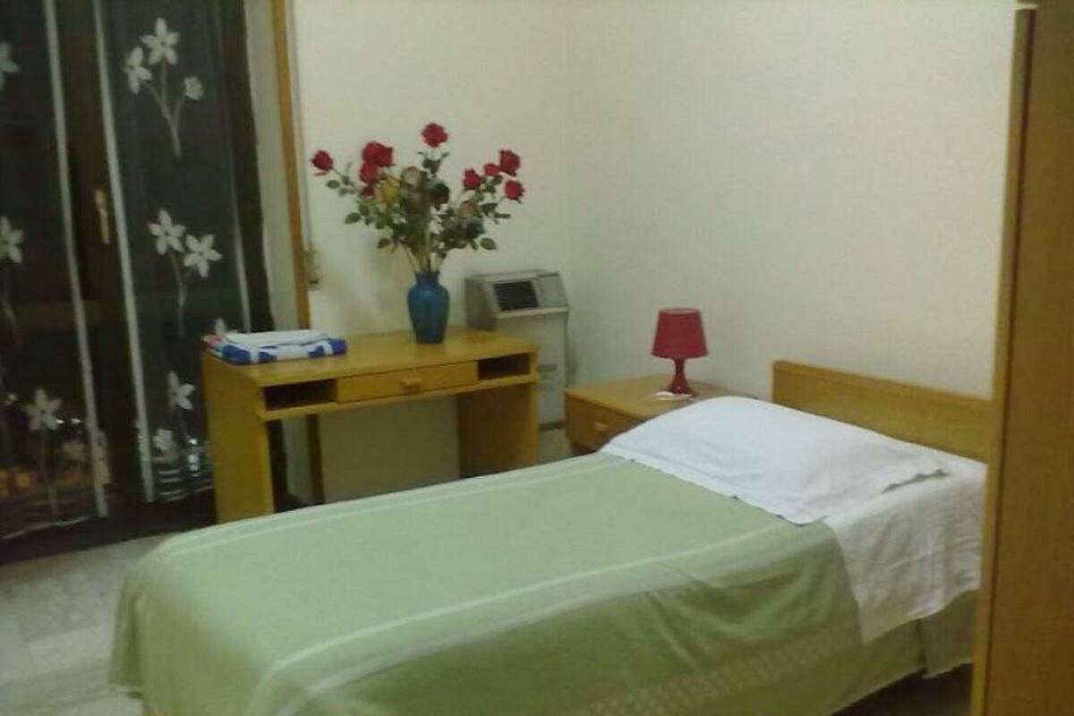 Une chambre à coucher avec un lit, un bureau, une chaise, une lampe et un vase de fleurs.