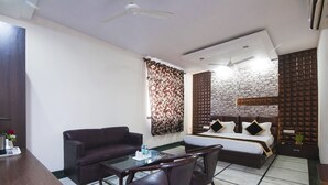 Habitació d'hotel moderna amb llit, sofà, taula de dinar amb cadires i una taula auxiliar petita.