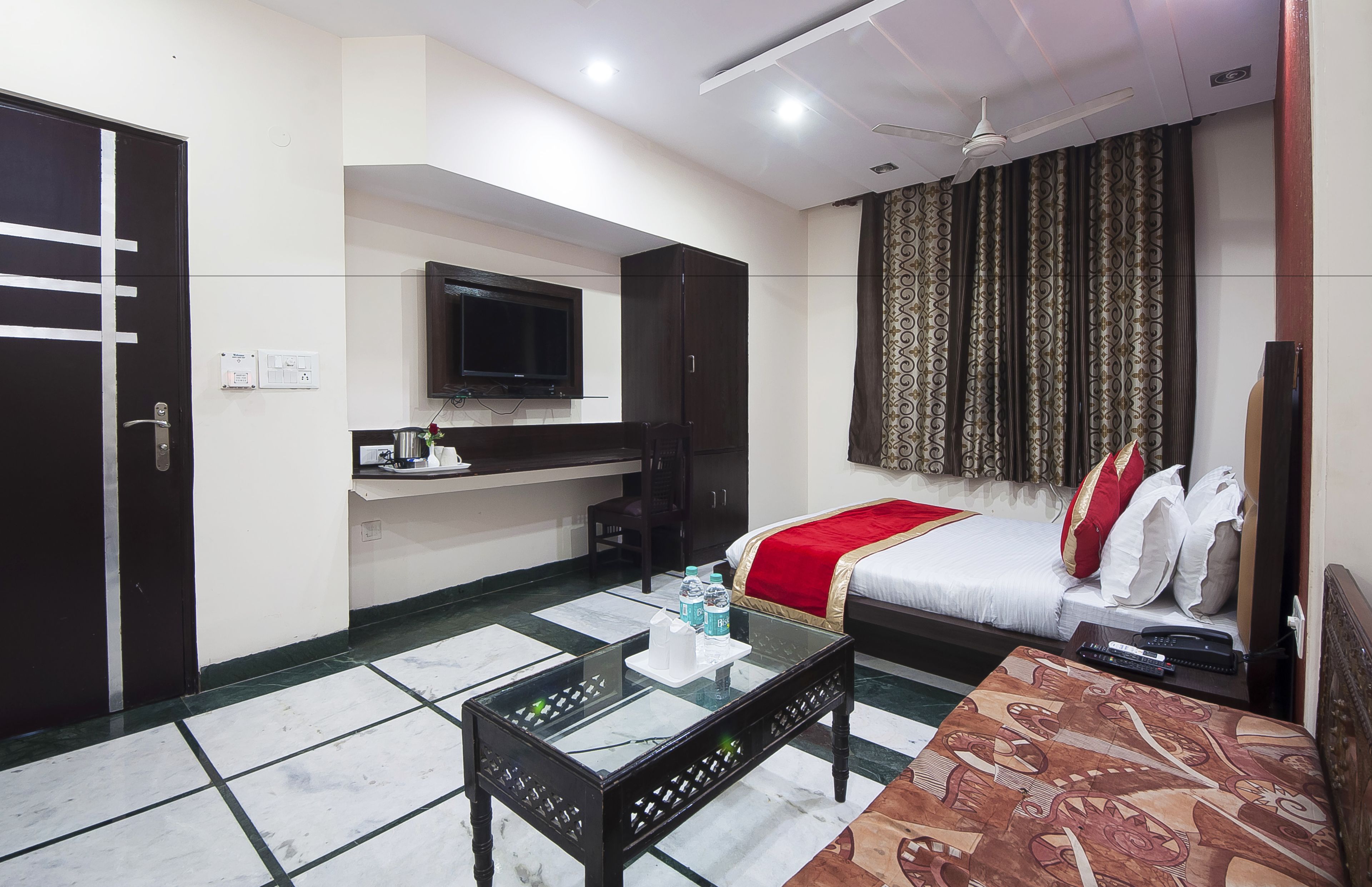 A hotel room with a bed, a TV mounted on the wall, a small table with a tray, and a ceiling fan.