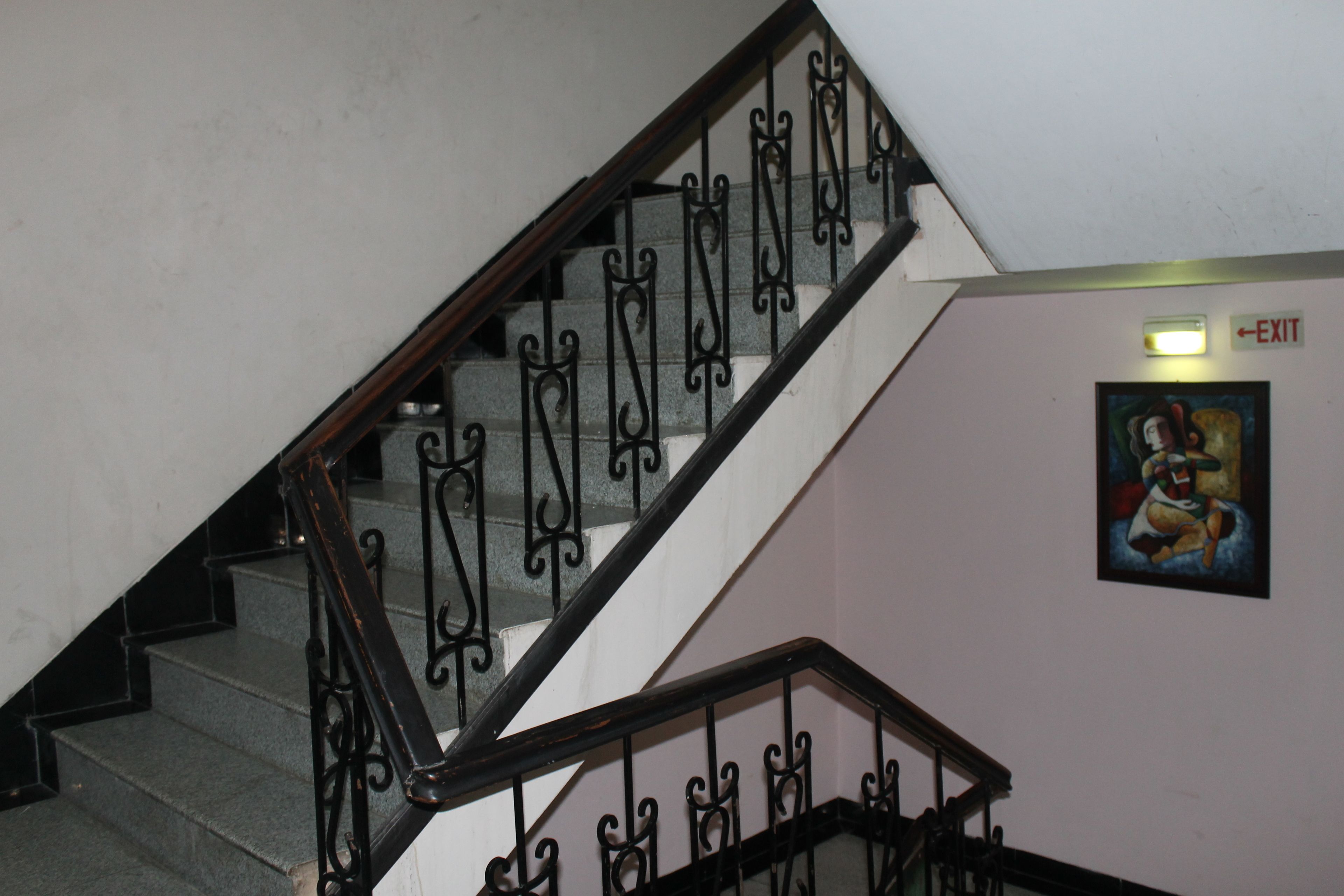 A staircase with ornate black railings and a wall-mounted exit sign.