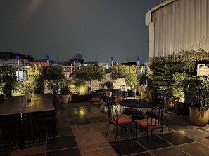 An outdoor patio area with tables and chairs, surrounded by potted plants and illuminated by blue lights. - Hotel Pooja Palace (New Delhi)