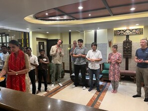 A group of people standing in a lobby with a reception desk, a green sofa, and a decorative wall. - Hotel Pooja Palace (New Delhi)