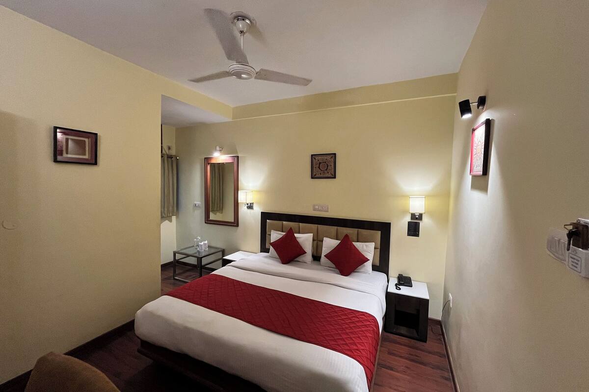 A hotel room with a bed, bedside tables, a ceiling fan, and wall-mounted lights.