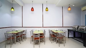 A restaurant with multiple tables and chairs, hanging pendant lights, and an air conditioning unit. - Hotel Pooja Palace (New Delhi)