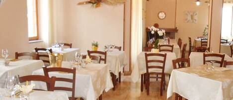 A restaurant with multiple tables covered with white tablecloths, wooden chairs, and a wooden floor.