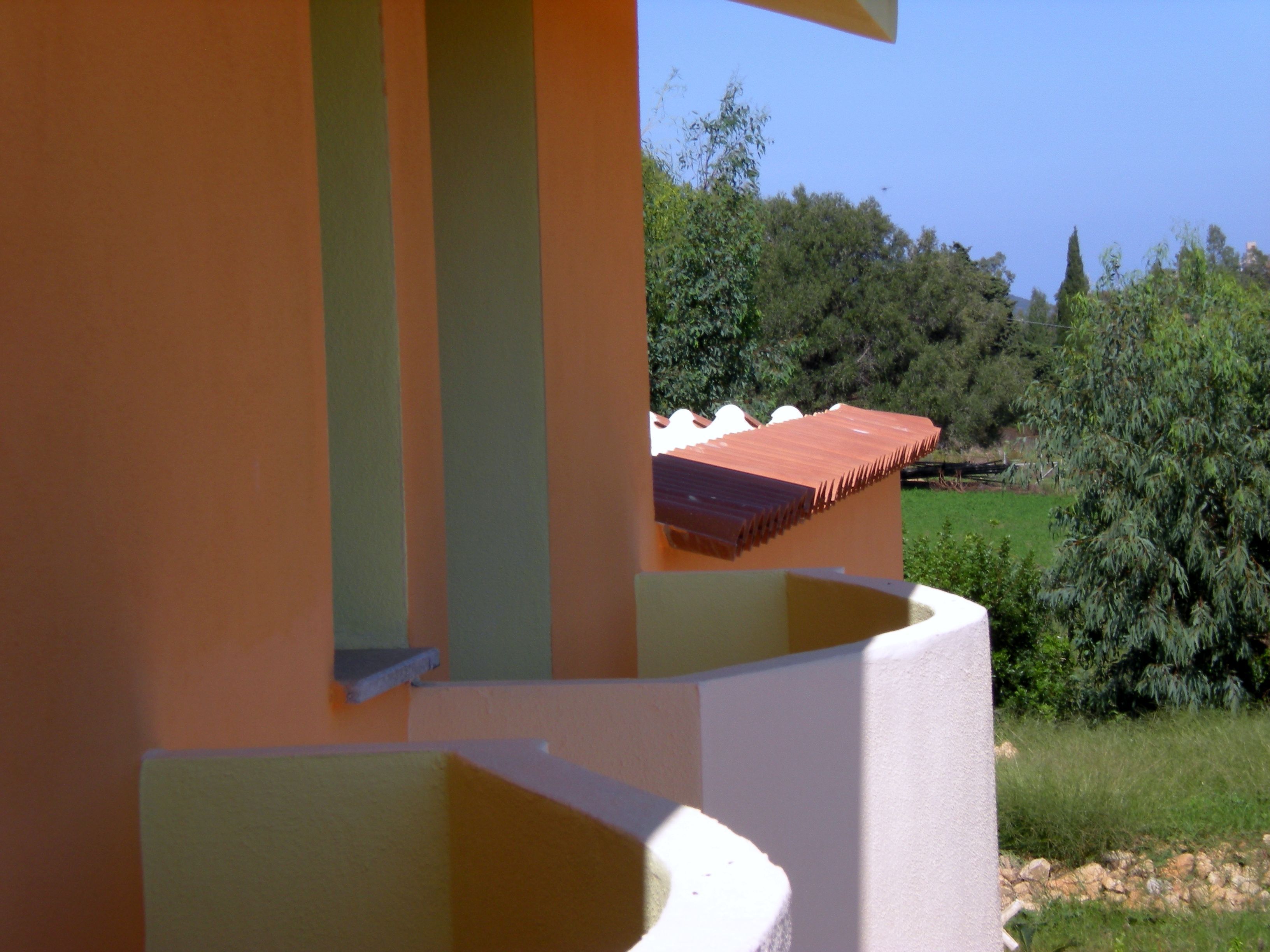 A modern building with a sloped roof and a view of a green landscape with trees and a clear sky.
