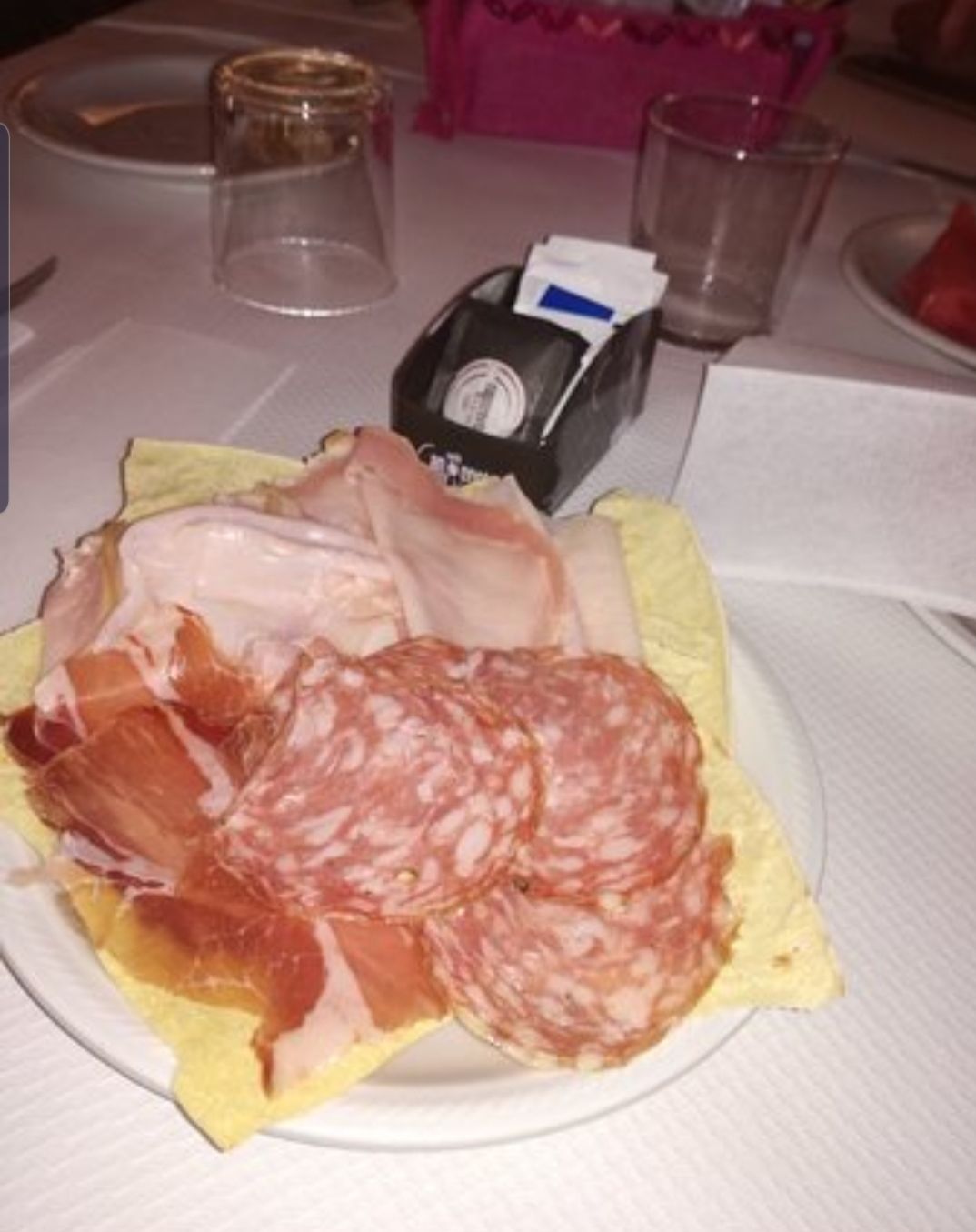 A plate with sliced meats and a small packet of condiments on a table.